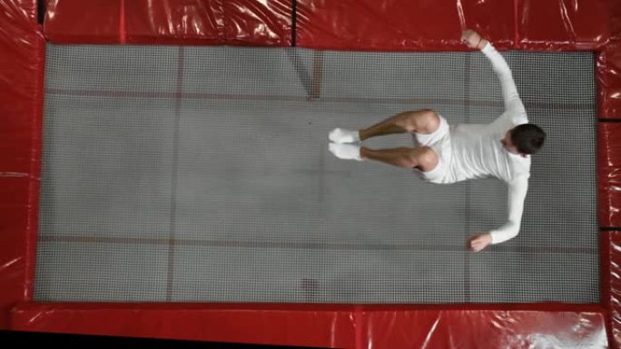 穿着白色衣服的俯视图体操运动员杂技演员在蹦床上进行慢动作翻筋斗