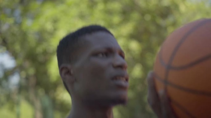 集中的非洲裔美国运动员将球扔进篮球架的特写镜头。夏天热衷于户外运动训练的坚定年轻人的肖像。
