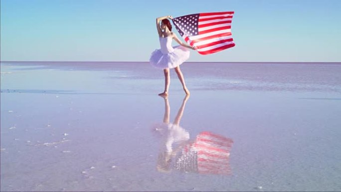 美丽的芭蕾舞演员在水上举着美国国旗。有风的一天。慢动作