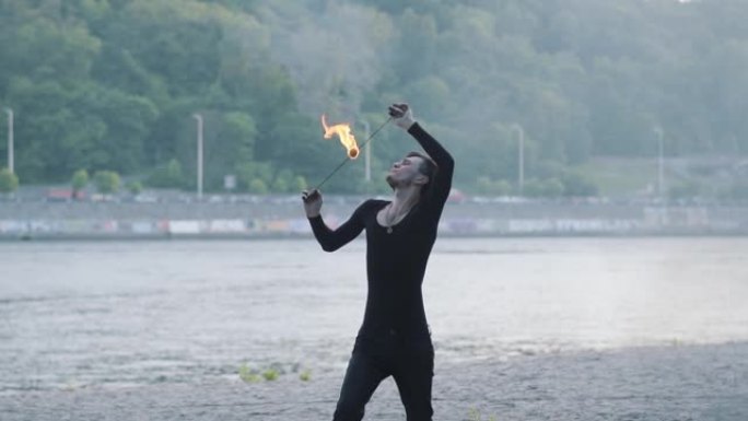 穿着黑色衣服的年轻人在河岸上站着火焰表演。