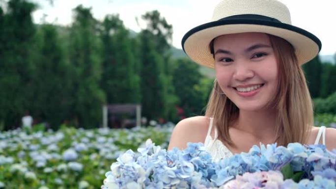 泰国美女，她拿着绣球花花束对着镜头微笑，游客她去了绣球花场。新鲜空气，她很开心