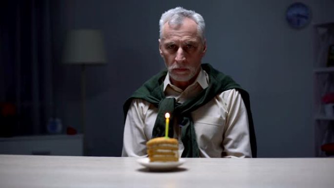 沮丧的老人看着生日蛋糕，独自在家庆祝假期
