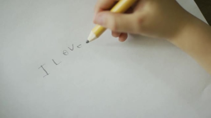 一名白人五岁孩子的手在纸上用铅笔写下 “我爱达达”
