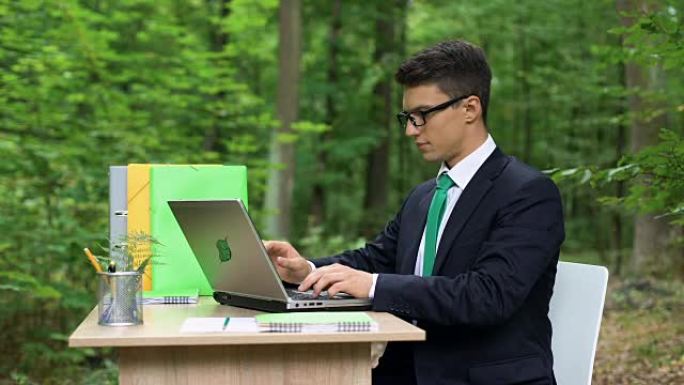 穿着西装的快乐男人在绿色美丽的森林中完成工作并放松
