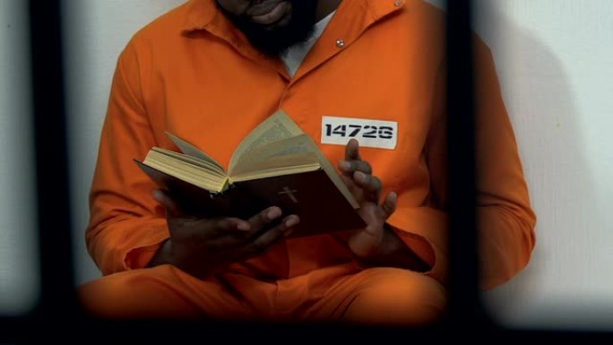 黑人男性囚犯在牢房里阅读圣经，希望得到宽恕，忏悔