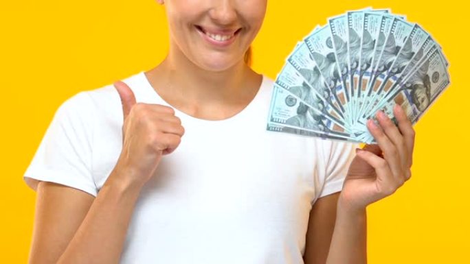 快乐的女士拿着一堆美元，露出大拇指，薪水和福利