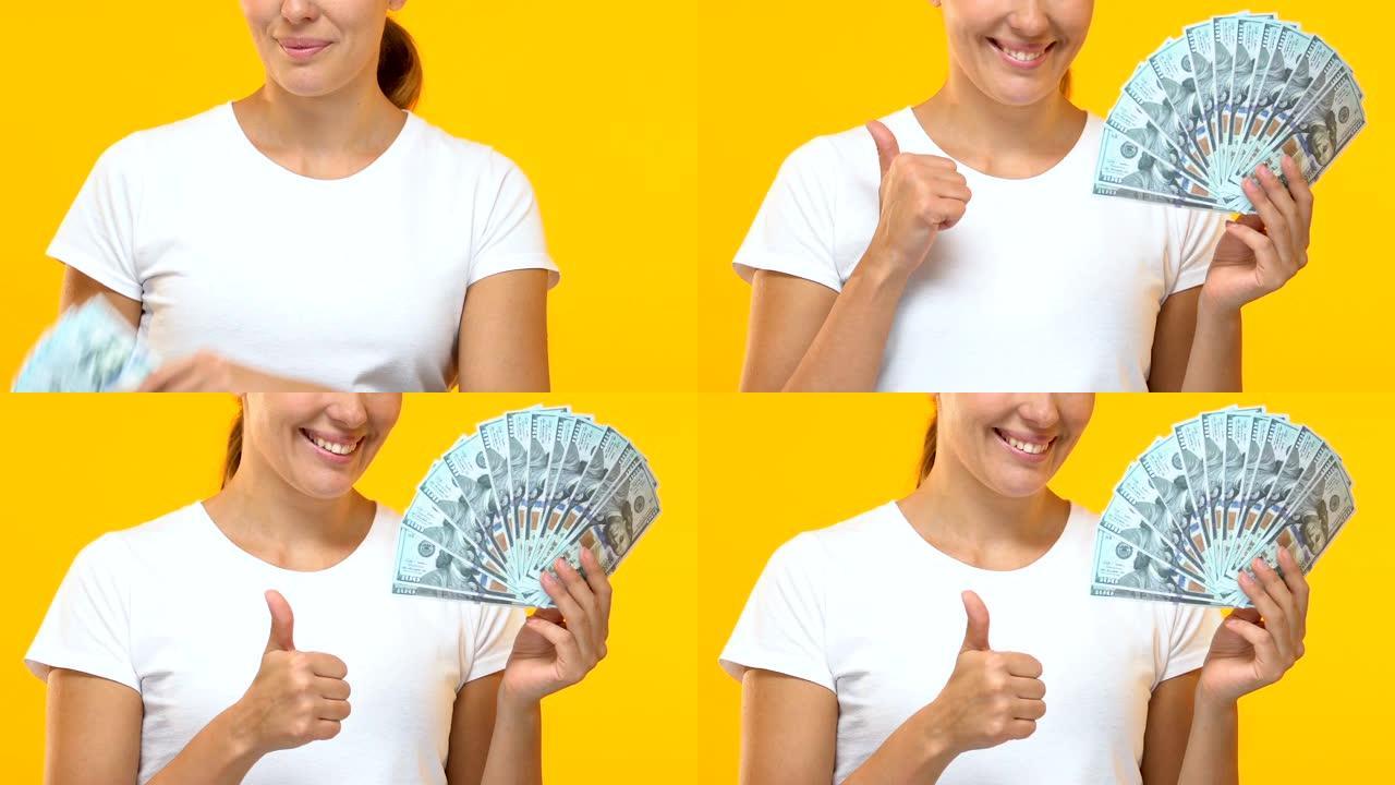 快乐的女士拿着一堆美元，露出大拇指，薪水和福利