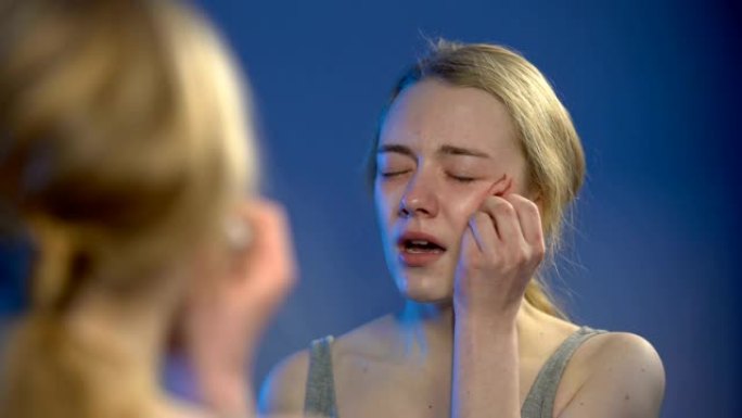 哭泣的年轻女子在镜中消毒脸部伤口，问题绝望