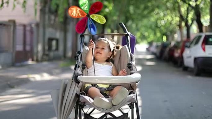 婴儿坐在婴儿车里玩彩虹风车，风车