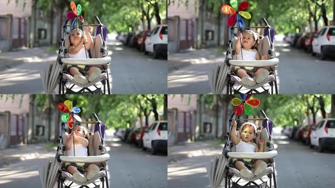婴儿坐在婴儿车里玩彩虹风车，风车