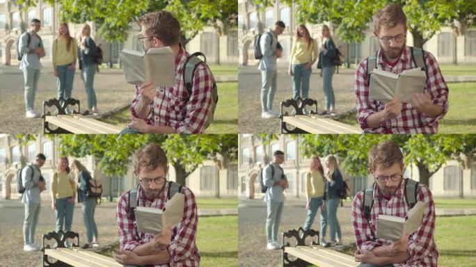 害羞的白人大学生戴眼镜，遭受同伴的欺凌。年轻的大胡子男人坐在长凳上的肖像，书当模糊的人在背景上大笑。
