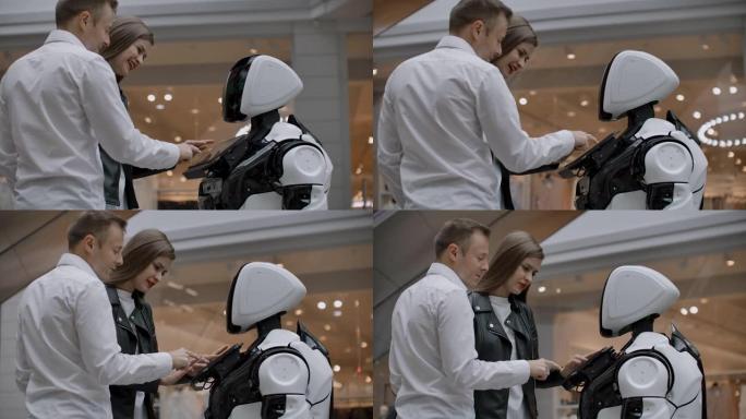 两人一男一女与机器人交流。用手在屏幕上按下机器人。在购物中心与一对夫妇互动的机器人助手。