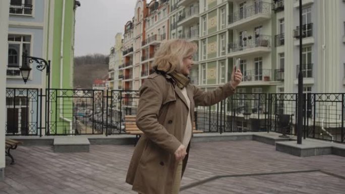积极的高级白人妇女在户外自拍相机上挥手交谈。快乐的退休人员在外国城市享受秋日。旅游，旅游，生活方式。