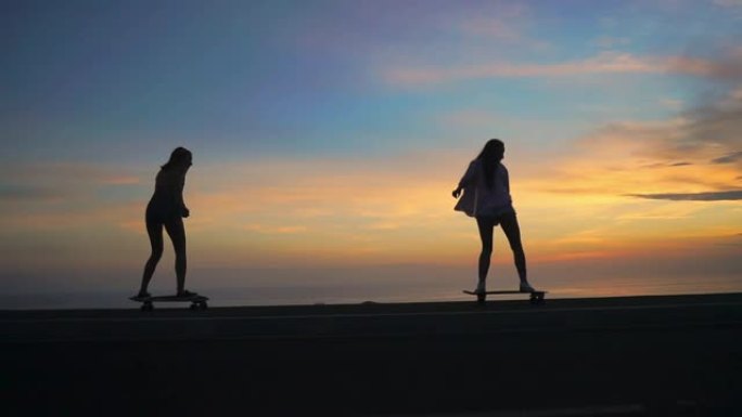 海洋和日落天空背景下两个女孩骑滑板的剪影