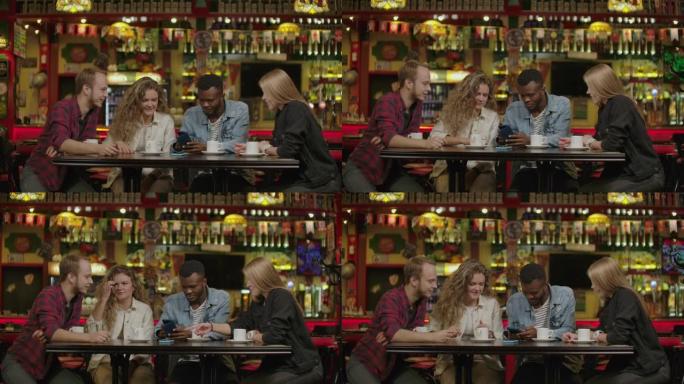 快乐的年轻朋友坐在咖啡馆里看着智能手机的肖像。混合种族的人坐在餐厅的桌子旁使用手机。