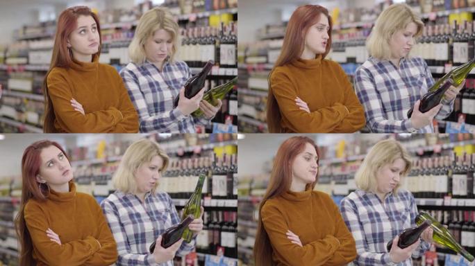无聊的红发白人女人在商店里等着女性朋友在红酒和白葡萄酒之间做出选择。年轻迷人的女孩在超市买饮料。生活
