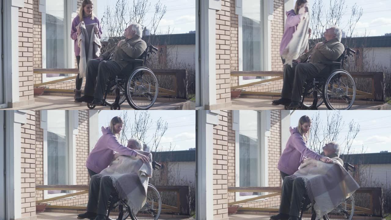 戴眼镜的白人妇女为坐在轮椅上的残疾老人带毯。护士照顾享受阳光明媚的秋日的老退休人员。帮助，帮助，支持