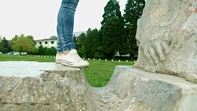 在城市公园中，女性双腿从石头跳到石头的近距离追踪镜头