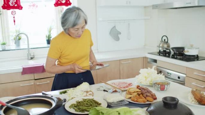 资深亚洲女性按照平板电脑上的食谱在家做饭