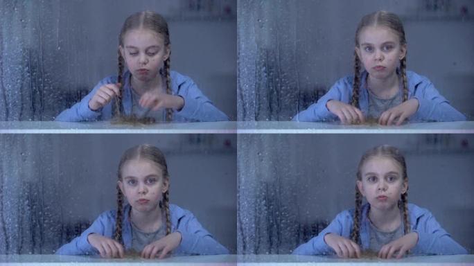 无聊的小女孩在下雨的天气里透过窗户看着相机，孤独
