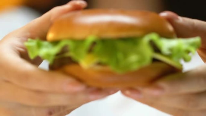 年轻女子的手的特写镜头显示汉堡进入相机，美味的垃圾食品