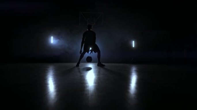 一名男子在黑暗的篮球场上，在烟雾中的篮球环的背景下，展示了由三个灯笼照亮的运球技巧。