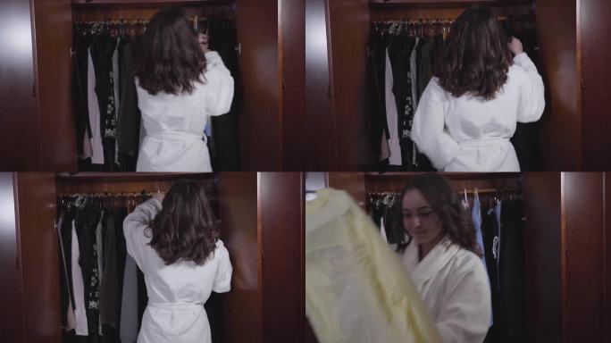 年轻的黑发女人站在敞开的衣柜前，早上选择衣服。漂亮女人扔衣服，拿着黄色衬衫离开。生活方式，幸福。