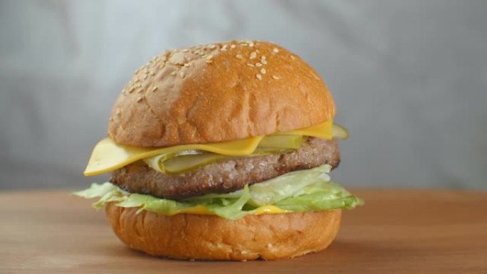汉堡在木板上旋转。一个汉堡配肉排沙拉奶酪和西红柿，靠在灰色的墙上。