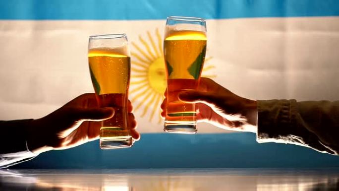 两名男子在阿根廷国旗的背景下碰碰啤酒杯，慢动作