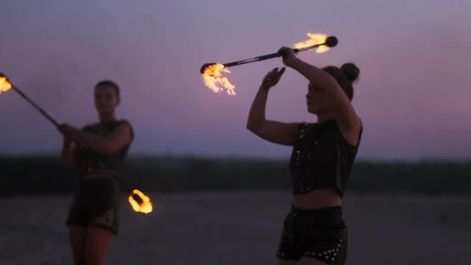 日落时分，在沙滩上放火的妇女跳舞，并以慢动作向美丽的天空展示技巧。