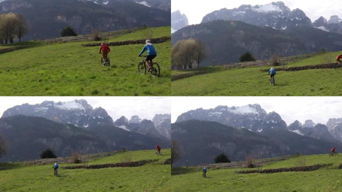 年轻的男人和女人骑自行车穿越绿色的草地，在山下