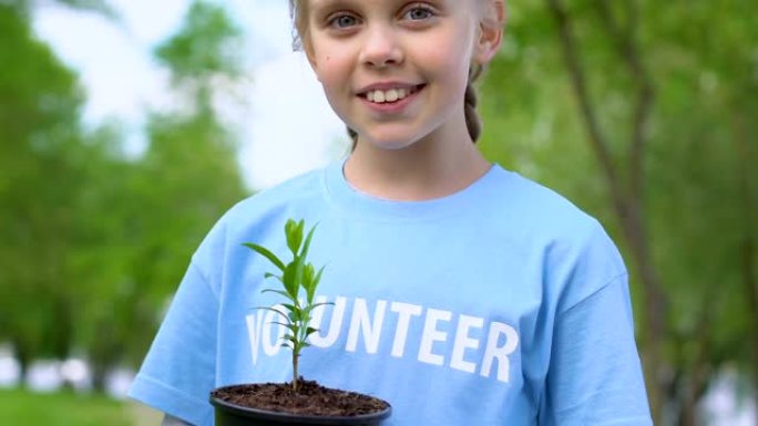 漂亮的小女孩抱着植物树苗，在镜头前微笑，生态志愿服务