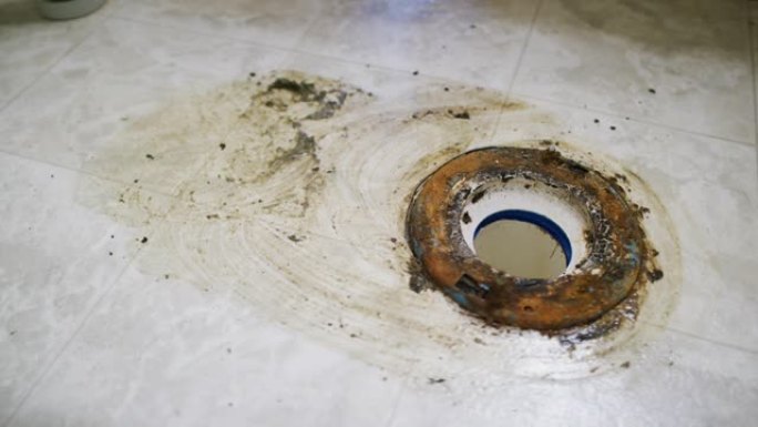 一名高加索修理工用刷子和纸巾清洁室内家庭浴室中拆除的马桶下的地板