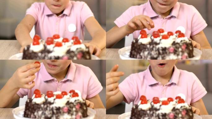 快乐的男孩从奶油蛋糕上吃樱桃，不健康的饮食，肠胃病学
