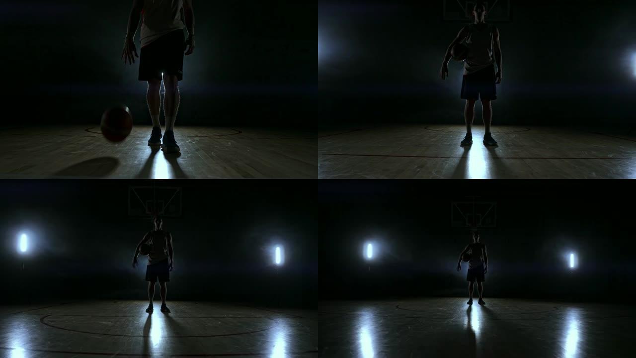 穿着运动服的篮球运动员穿着红色短裤和蓝色t恤在黑暗的篮球场上，从烟雾中冒出来，在慢动作中看着相机