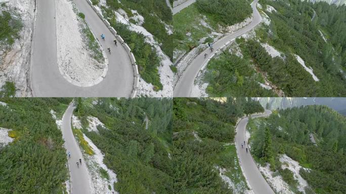 空中三个公路自行车手在俯瞰山脉和森林的道路上下山