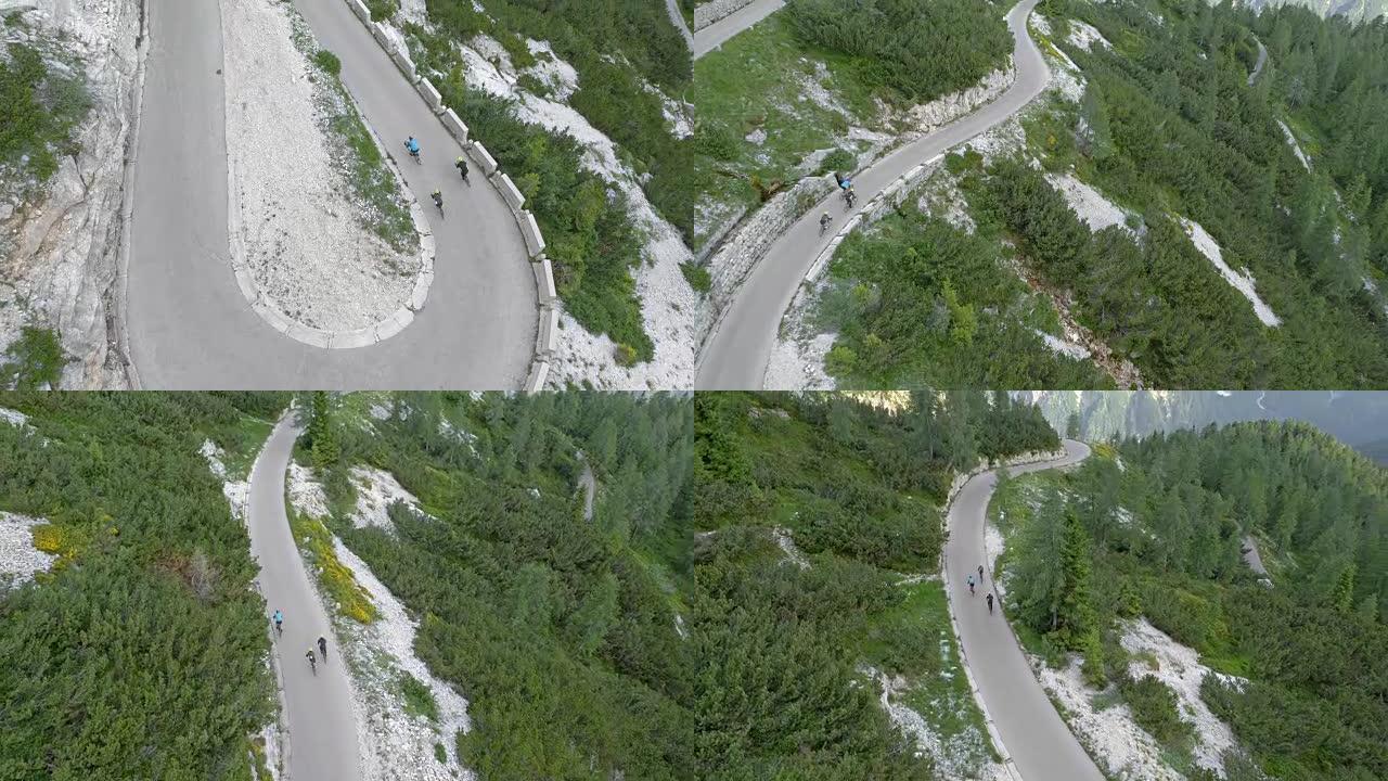 空中三个公路自行车手在俯瞰山脉和森林的道路上下山