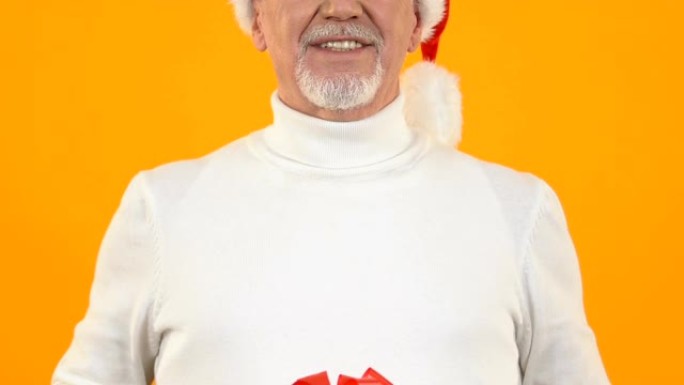 戴着圣诞老人帽子的快乐成熟男人展示红丝带礼物，礼物惊喜