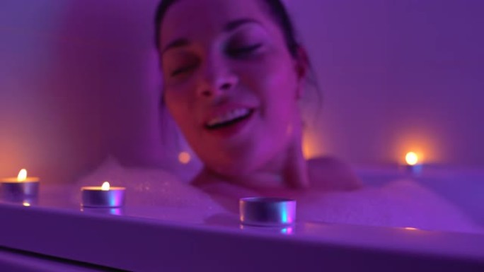 兴奋的女人在泡沫浴缸里放松，吹蜡烛，浪漫的夜晚