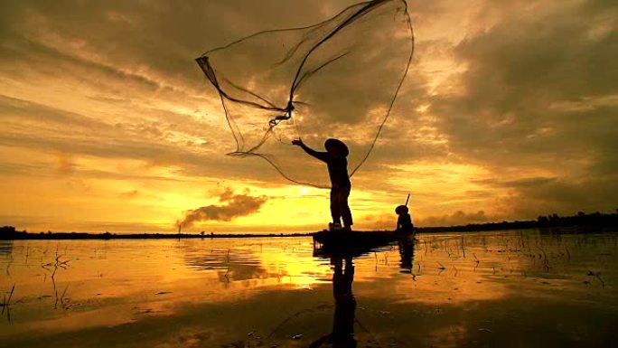 高清: 剪影亚洲渔民在木船上撒网，在日出前的清晨在自然河中捕捞淡水鱼