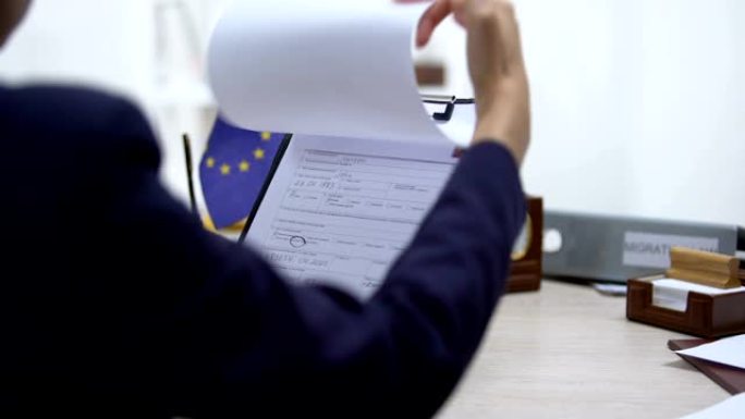 移民检查员拒绝签证申请，桌上放着欧盟旗帜