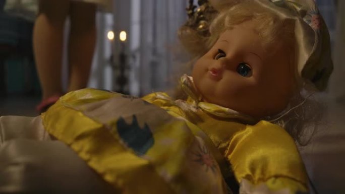 烛光下躺在地板上的奇怪洋娃娃的特写。白人小女孩的脚站在背景下。恐惧，恐惧，奇怪。