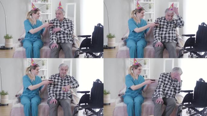 善良的白人妇女在疗养院给白发老人送生日蛋糕。沮丧的退休人员脱下党帽，用手握住头。悲伤，沮丧，衰老。