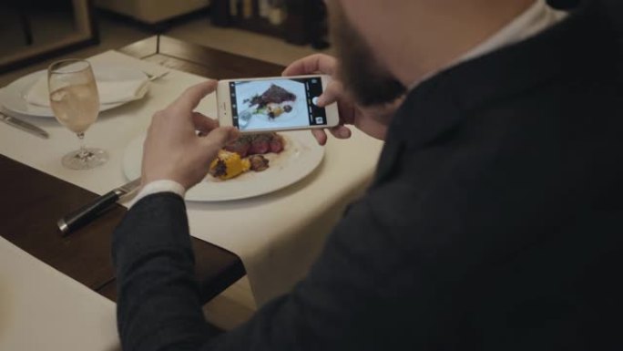 男性坐在餐厅的桌子上，在盘子上拍大牛排的照片。