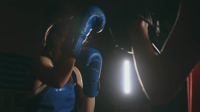 女拳击手在烟雾弥漫的体育馆里用拳击手套拳打焦点手套
