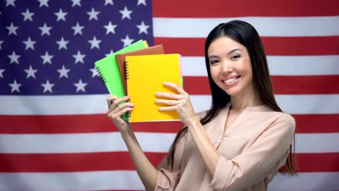 亚洲女孩在美国国旗背景下微笑，学生拿着抄写本
