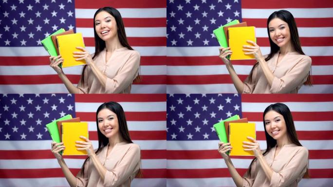 亚洲女孩在美国国旗背景下微笑，学生拿着抄写本