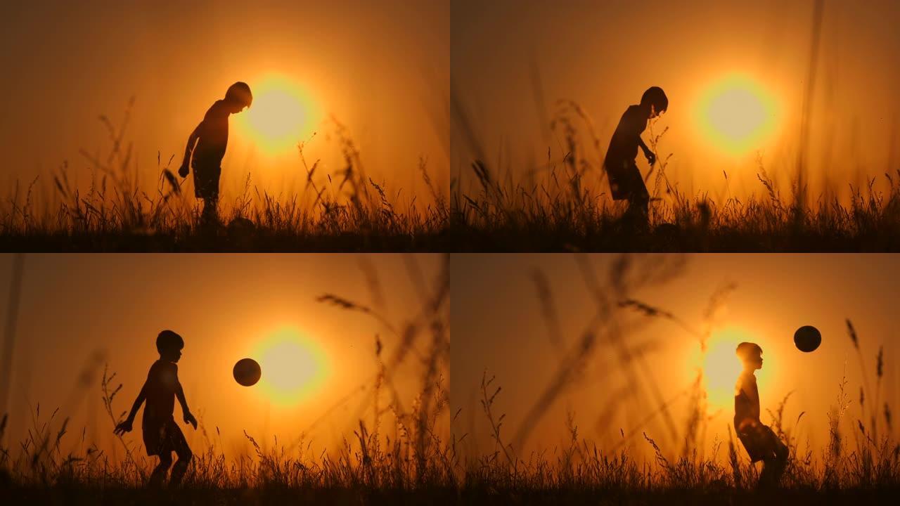 小男孩足球运动员剪影，男孩在日落时在球场上玩杂耍。慢动作。