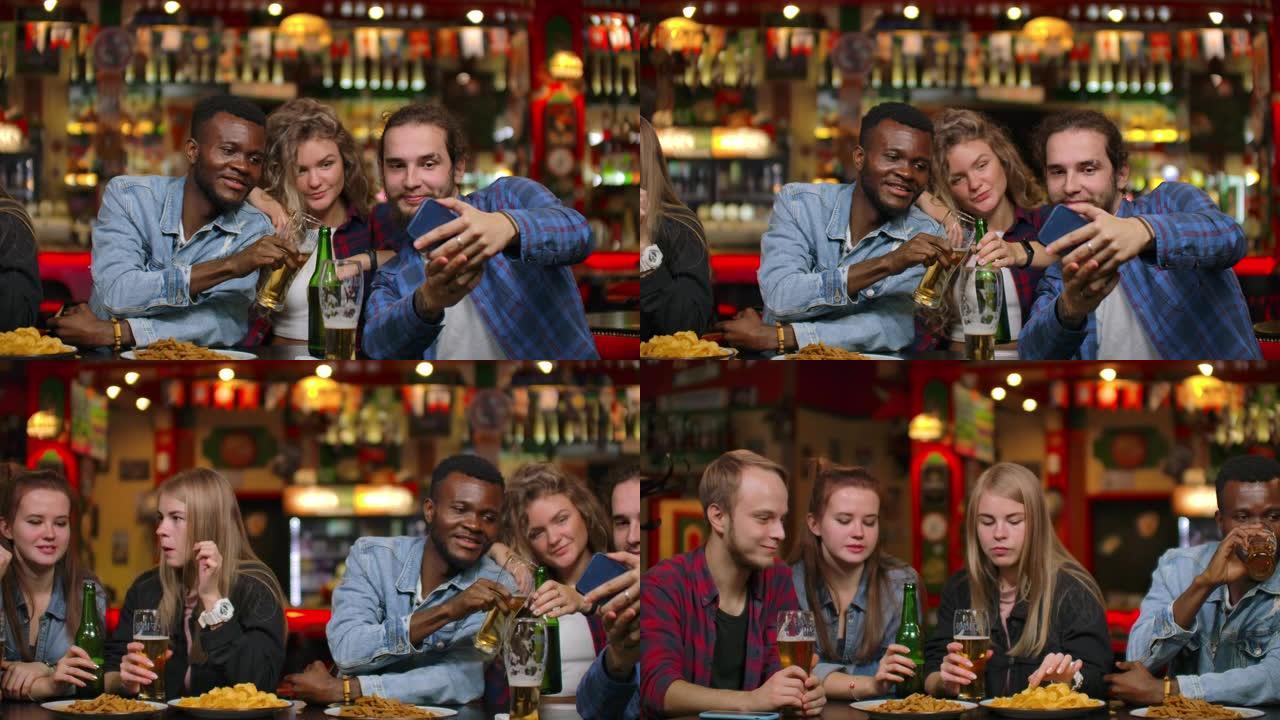 非裔美国人和欧洲朋友坐在酒吧里自拍。一大群朋友坐在一张桌子上的酒吧里聊天，喝啤酒和拍照
