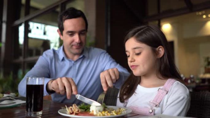 爱心爸爸帮助女儿在酒店餐厅切食物